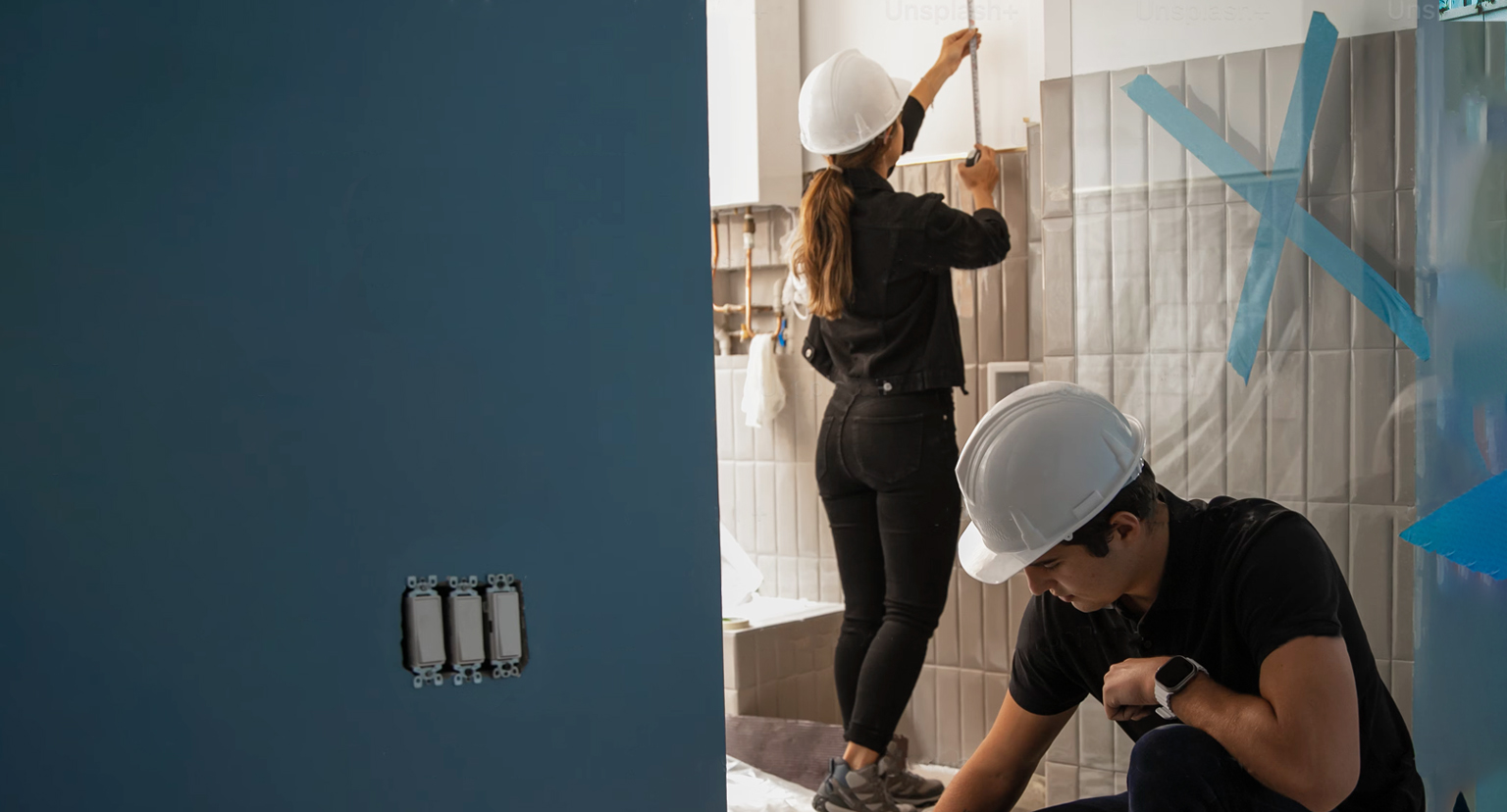 Two construction workers are working on a bathroom.