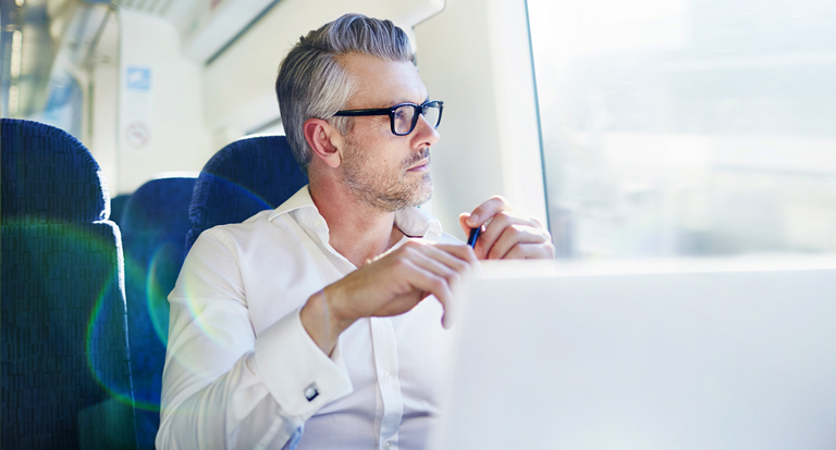 A man sitting on a train looking at his laptop.