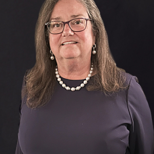 A woman with glasses and pearls smiling for the camera.