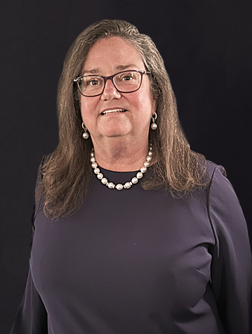 A woman with glasses and pearls smiling for the camera.