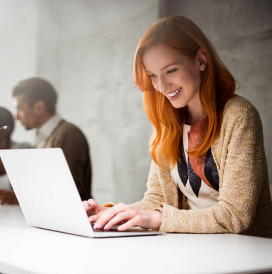 A woman with red hair is using a laptop in an office.