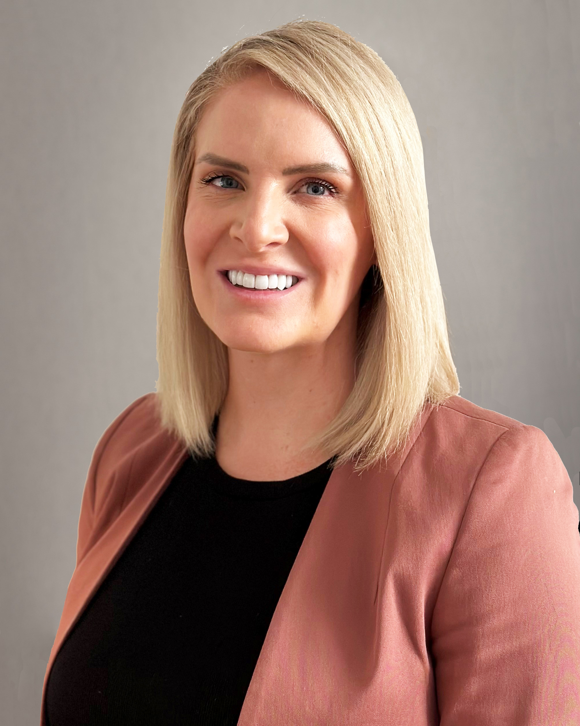 Portrait of a woman with shoulder-length blonde hair, wearing a black top and a light brown blazer, smiling against a neutral background.